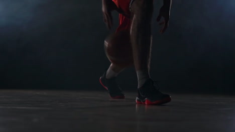 Male-athlete-in-sportswear-and-sneakers-prokipyvaet-basketball-ball-between-legs-on-the-basketball-court-in-the-smoke-in-slow-motion